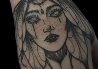 Tatouage sur la main représentant un visage sur le dos d'un papillon. Style de tattoo néo tribal