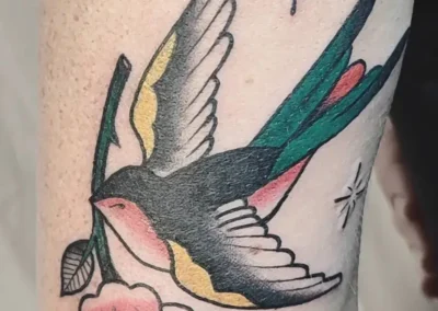 Tatouage hirondelle old school portant une fleur dans son bec