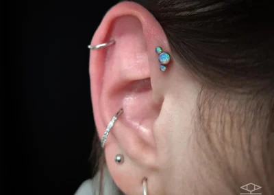 Oreille d'une jeune femme avec 5 piercing. Piercing forward hélix avec un bijou bleu, un anneau au niveau de l'hélix, un anneau à la conch et de bijoux sur le lobe