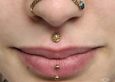 Femme avec un bijou de piercing sur chaque narine, rejoint par une chaine. Piercing médusa et piercing sur la lèvre inférieure