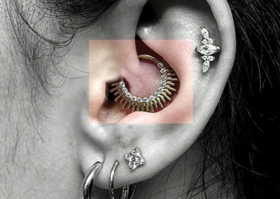 Oreille avec 4 bijoux de piercing. 2 piercing sur le lobe, 1 piercing daith et 1 piercing helix