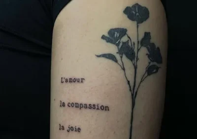 Tatouage sur le bras, d'une fleur et d'écritures en style blackwork