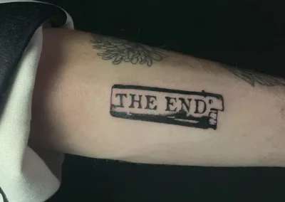 Tatouage blackwork sur l'avant-bras d'une personne, représentant le texte "THE END" dans un cadre rectangulaire