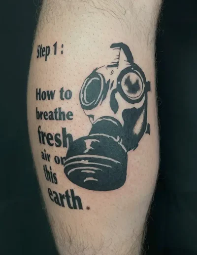 Tatouage blackwork sur un mollet, représentant un masque à gaz vintage détaillé à côté du texte "Step 1: How to breathe fresh air on this earth