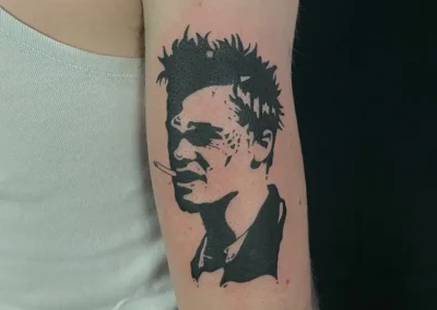Tatouage blackwork sur un bras représentant un homme aux cheveux hérissés avec une cigarette à la bouche