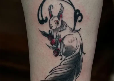 Tatouage d'un écureuil blanc, tenant des framboises rouges, style néo-traditionnel en noir, gris et rouge, sur la jambe