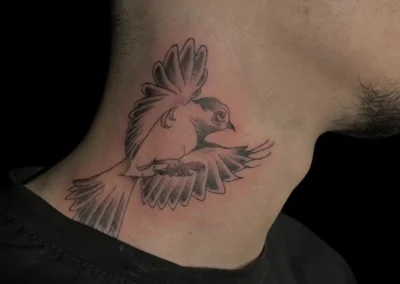 Tatouage d'un oiseau en vol, style dotwork et fineline en noir et gris, sur le côté du cou