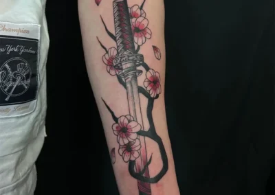 Tatouage de sabre japonais Katana avec des fleurs de cerisier roses et des pétales volants, style néo-traditionnel sur le bras