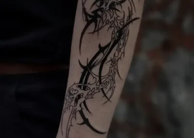 Tatouage abstrait style néotribal ou tribal moderne en noir, avec des formes organiques et pointues sur l'avant-bras