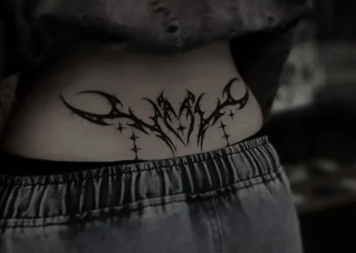 Tatouage abstrait style goth ou néotribal noir, sur le bas du dos, avec des formes pointues et des étoiles