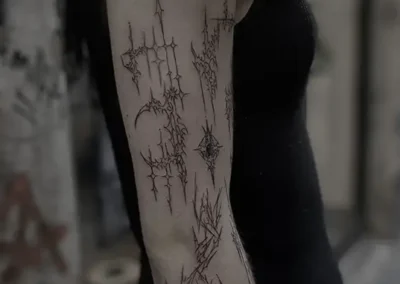 Tatouage abstrait style cyber sigilism ou blackwork, avec des motifs linéaires et des pointes, sur l'avant-bras