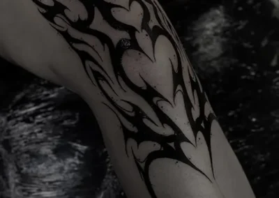 Tatouage style néotribal avec un motif abstrait de formes pointues et des cœurs, en noir sur le genou