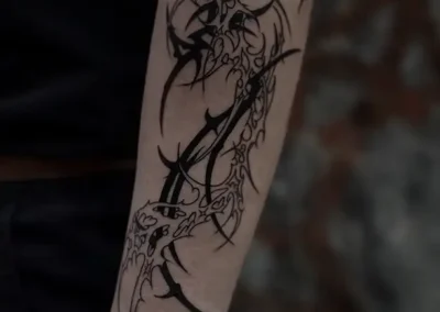 Tatouage abstrait style néotribal ou blackwork, avec des formes pointues et tentaculaires en noir sur l'avant-bras