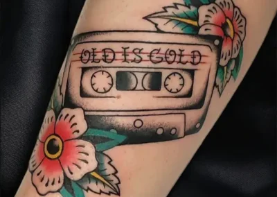 Tatouage avant-bras : cassette Old is Gold et fleurs style American Traditional