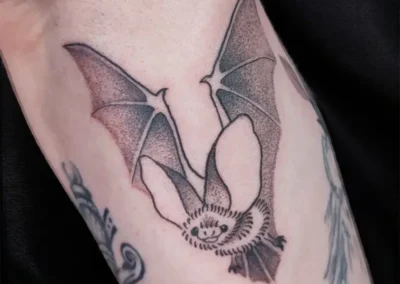 Tatouage de chauve-souris souriante et détaillée, ailes déployées, en monochrome