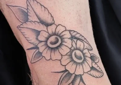 Tatouage traditionnel floral noir et gris, avec des fleurs simples et des feuilles stylisées