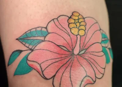Tatouage floral de fleur d'hibiscus stylisée, aux pétales roses et pistil jaune, sur une peau claire