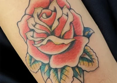 Tatouage de fleur de rose éclatante aux couleurs chaudes, avec contours noirs et ombrages