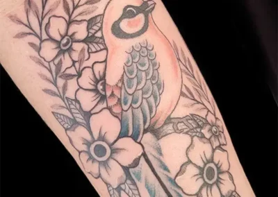 Tatouage détaillé d'un oiseau chantant sur un lit de fleurs et de feuillages, couleurs pastel et tons gris