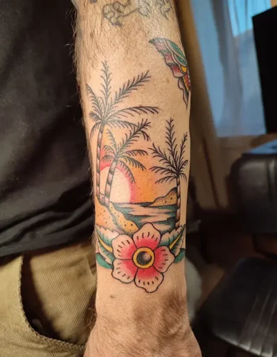 Tatouage old school paysage de plage avec palmier au coucher du soleil et fleur rouge sur le bras