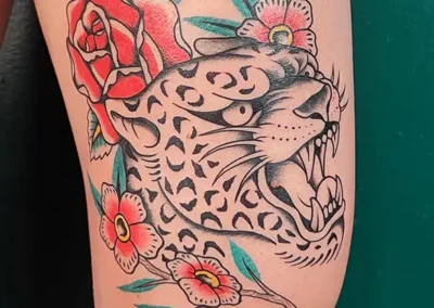 Tatouage animalier : panthère noire et gris avec des détails rouges et verts, inspiré du style américain traditionnel