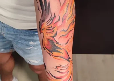 Tatouage phénix coloré en orange et jaune avec des flammes noires, sur l'avant-bras