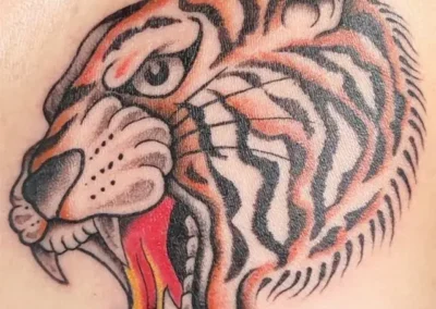 Tatouage tête de tigre rugissant en orange, noir et blanc, style traditionnel