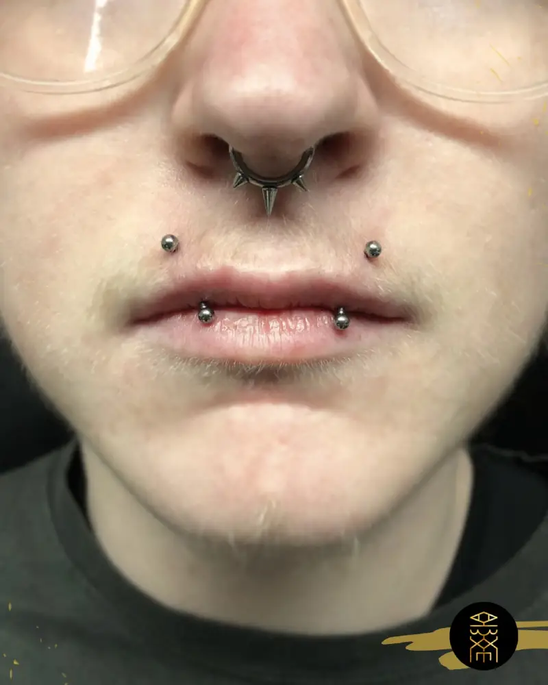 Piercing angel fangs Homme avec plusieurs piercings faciaux, dont un piercing au septum avec un bijou à pointes, et des piercings labiaux (angel fangs) avec des billes en métal