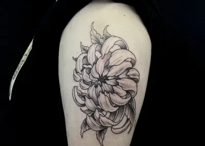 Tatouage d'une grande fleur de chrysanthème ou pivoine sur l'épaule, dans un style fineline et dotwork en noir et gris