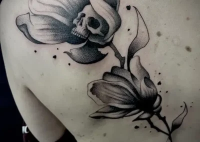 Tatouage d'une fleur avec une tête de mort dissimulée en son centre, dans un style réaliste en noir et gris dans le dos