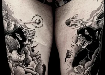 Tatouage d'inspiration japonaise, avec deux figures de démons ou loups-garous qui s'affrontent sur les deux cuisses, dans un style réaliste en noir et gris