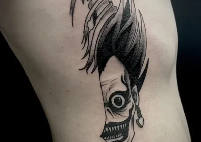 Tatouage du joker transforme en dague, dans un style sombre en noir et gris, sur le côté du corps