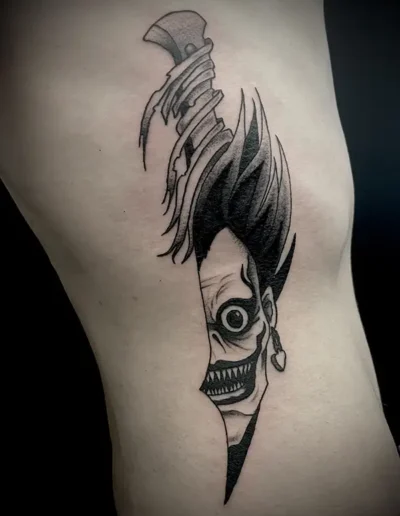 Tatouage du joker transforme en dague, dans un style sombre en noir et gris, sur le côté du corps