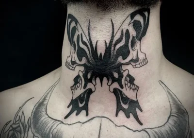 Tatouage d'un papillon de nuit avec des motifs de crânes sur chaque aile, en noir et gris, placé dans le cou