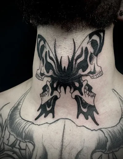 Tatouage d'un papillon de nuit avec des motifs de crânes sur chaque aile, en noir et gris, placé dans le cou
