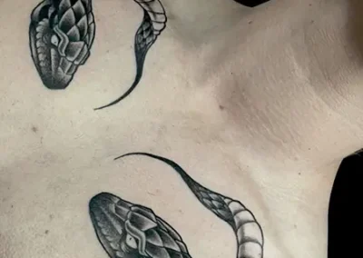 Tatouage d'un serpent enroulé en noir et gris, avec un motif d'écailles détaillé, s'étendant de l'épaule jusqu'à la clavicule