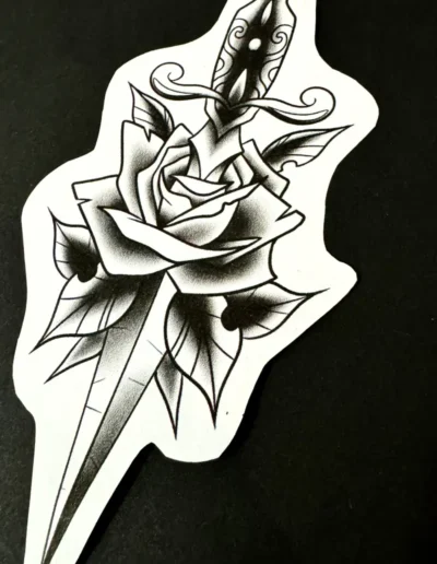 Dessin de tatouage flash, de style traditionnel américain ou néo-trad, représentant une rose et une dague transperçant la fleur, en noir et gris.
