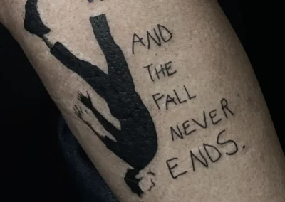 Tatouage sur un mollet : une silhouette humaine tombe à l'envers, avec le texte 'AND THE FALL NEVER ENDS.' tatoué à côté, en encre noire
