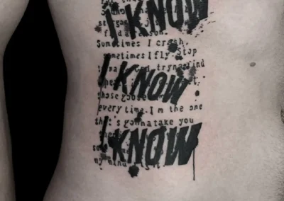 Tatouage sur les côtes avec un texte manuscrit superposé par trois grands 'I KNOW' de style graffiti noir intense