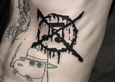 Tatouage sur les côtes montrant un symbole d'interdiction de style trash et dégoulinant à l'encre noire, situé au-dessus d'un personnage de dessin animé fumant