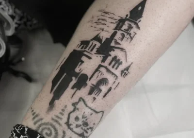 Tatouage noir style graphique sur un mollet représentant un château gothique avec texte manuscrit en fond