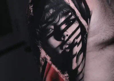 Tatouage visage de femme réaliste avec jeu d'ombres et touches de rouge style Trash Polka sur l'épaule