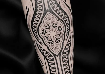 Tatouage ornemental et géométrique noir sur l'avant-bras avec motif mandala, lignes symétriques et dotwork