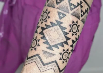 Tatouage ornemental et géométrique noir sur le haut du bras. Lignes symétriques et dotwork