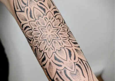 Tatouage ornemental et géométrique noir sur l'avant bras, motif mandala, lignes symétriques et dotwork