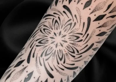 Tatouage ornemental et géométrique noir sur l'avant bras, motif mandala, lignes symétriques et dotwork