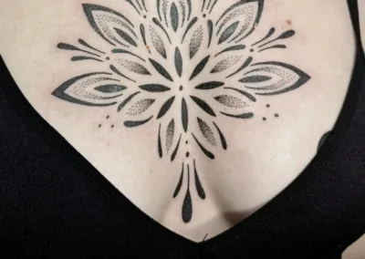 Tatouage ornemental et géométrique noir sur la poitrineavec motif mandala, lignes symétriques et dotwork