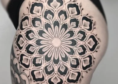 Tatouage ornemental et géométrique noir sur la cuisse, motif mandala, lignes symétriques et dotwork