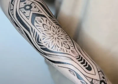 Tatouage ornemental et géométrique noir sur l'avant-bras avec motif mandala, lignes symétriques et dotwork