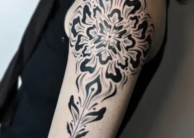 Tatouage ornemental et géométrique noir sur le haut du bras, motif mandala, lignes symétriques et dotwork